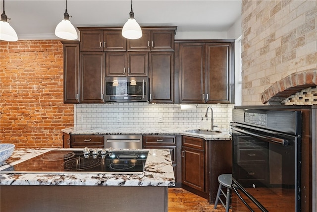 kitchen with a sink, black appliances, dark brown cabinets, hanging light fixtures, and brick wall