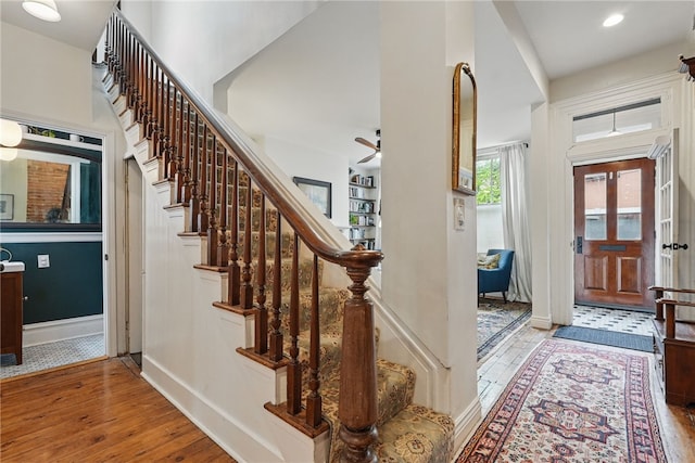 foyer entrance with hardwood / wood-style floors, stairway, a ceiling fan, and baseboards