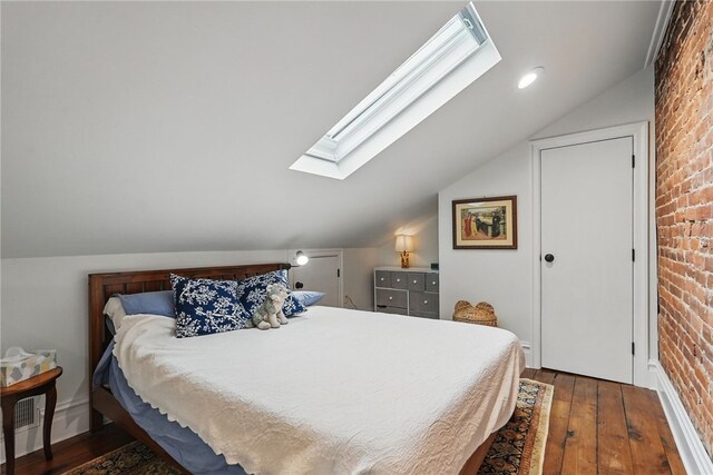 bedroom featuring a skylight, vaulted ceiling, brick wall, and wood-type flooring