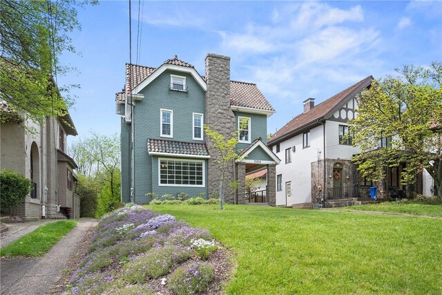 back of property featuring a lawn, a chimney, brick siding, and a tile roof