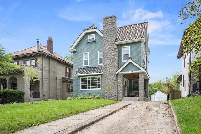 view of front of property with a tiled roof, a front yard, stone siding, and a chimney