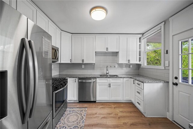 kitchen featuring stainless steel appliances, a sink, light stone countertops, tasteful backsplash, and white cabinetry