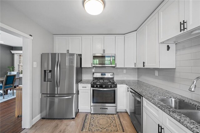 kitchen with stainless steel appliances, a sink, white cabinetry, and light wood-style floors