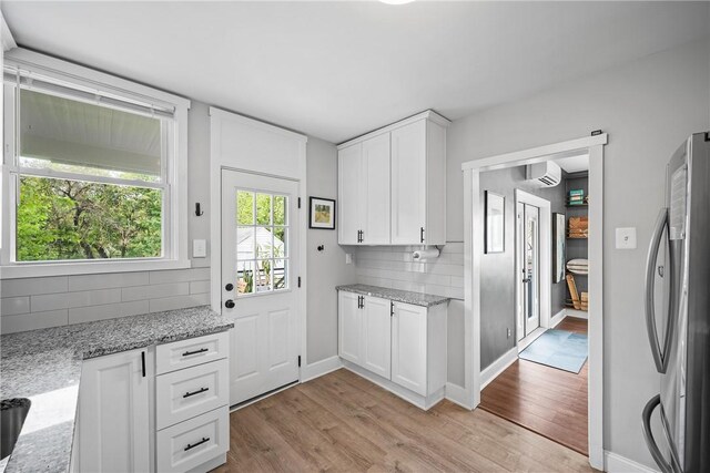 kitchen featuring freestanding refrigerator, light wood-style flooring, backsplash, and light stone countertops