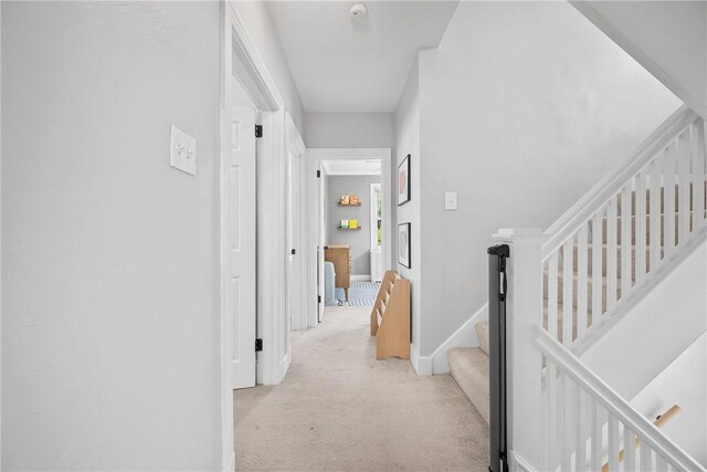 hall with light carpet, baseboards, and stairway