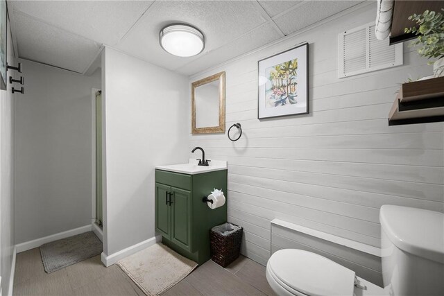 bathroom featuring toilet, wooden walls, vanity, a stall shower, and baseboards