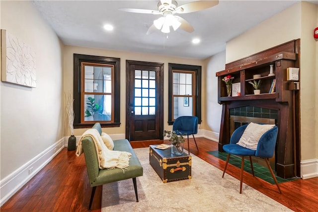 sitting room featuring baseboards, wood finished floors, a ceiling fan, a tiled fireplace, and recessed lighting