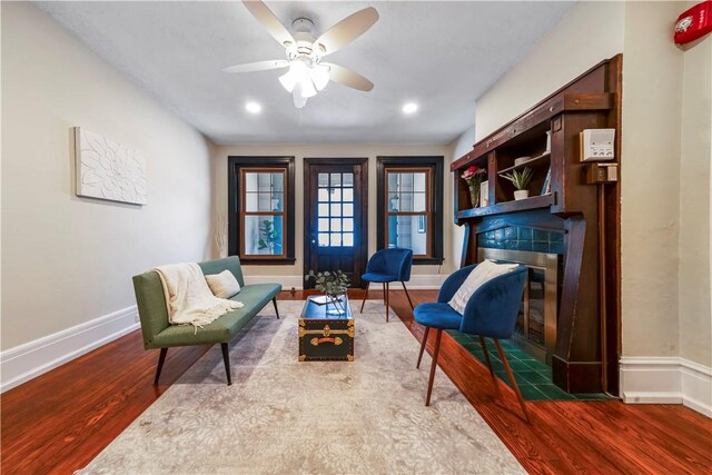 sitting room featuring a tile fireplace, wood finished floors, baseboards, and a ceiling fan