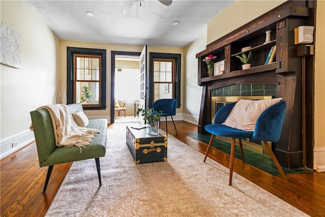sitting room featuring baseboards, wood finished floors, ceiling fan, a tile fireplace, and a textured ceiling