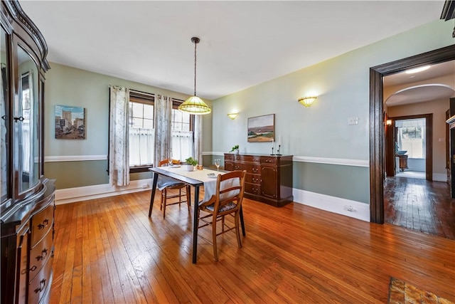 dining room with arched walkways, wood-type flooring, plenty of natural light, and baseboards
