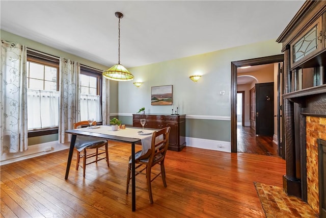 dining room with hardwood / wood-style flooring, arched walkways, a brick fireplace, and baseboards