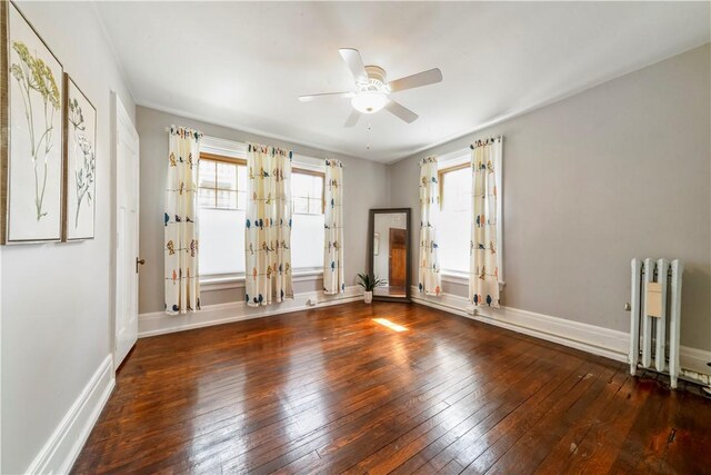 empty room featuring radiator, hardwood / wood-style flooring, a ceiling fan, and baseboards