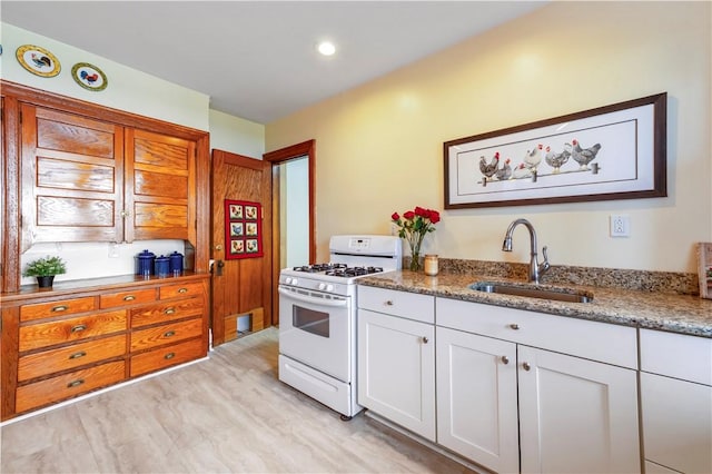 kitchen featuring a sink, white gas stove, light stone countertops, and white cabinetry