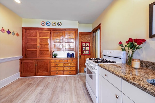 kitchen featuring white gas range, light stone countertops, white cabinets, light wood-style floors, and baseboards