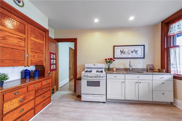 kitchen featuring white range with gas stovetop, a sink, baseboards, dark stone countertops, and recessed lighting