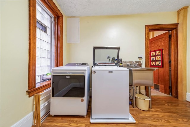 laundry room with washing machine and clothes dryer, light wood finished floors, healthy amount of natural light, and a textured ceiling