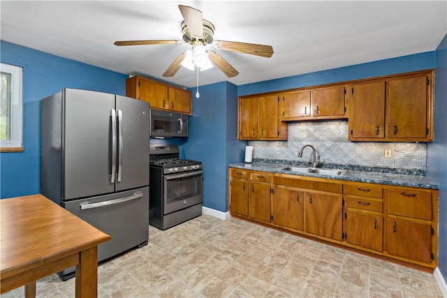 kitchen with stainless steel appliances, a sink, brown cabinetry, decorative backsplash, and a ceiling fan