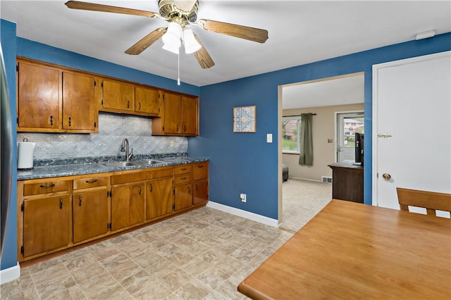 kitchen with a sink, brown cabinetry, ceiling fan, backsplash, and baseboards
