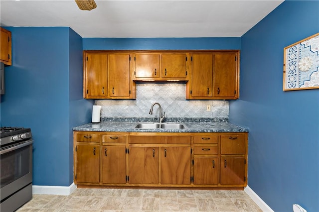 kitchen with a sink, stainless steel gas range, baseboards, and dark countertops