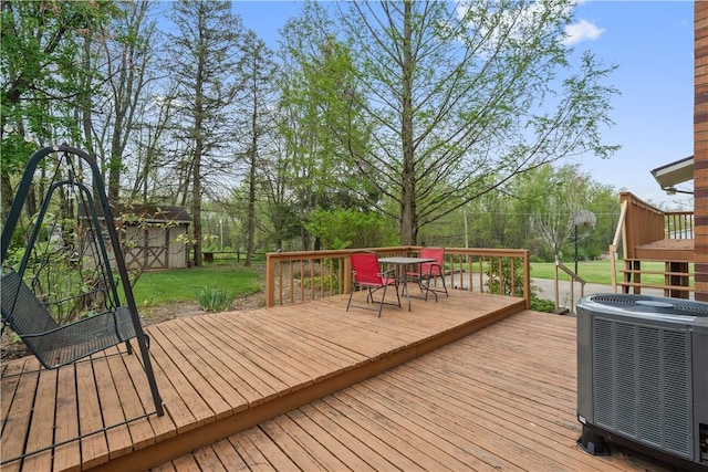 deck with central air condition unit, outdoor dining space, an outdoor structure, a lawn, and a shed