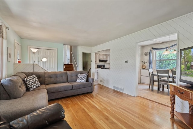 living area featuring light wood-type flooring, stairs, and wood walls