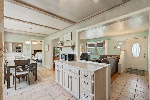 kitchen with light tile patterned flooring, stainless steel microwave, beamed ceiling, light countertops, and hanging light fixtures