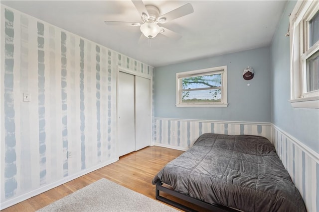 bedroom featuring wood finished floors, a wainscoted wall, ceiling fan, and a closet