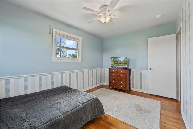 bedroom featuring wood finished floors, a wainscoted wall, and a ceiling fan