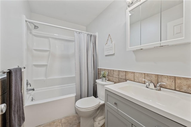 bathroom featuring tile walls, toilet, shower / bath combination with curtain, vanity, and a wainscoted wall