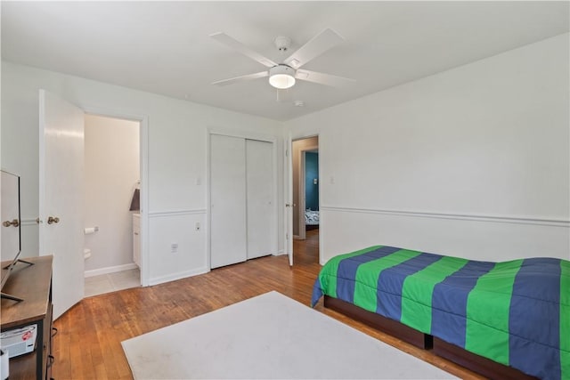 bedroom featuring wood finished floors, baseboards, ceiling fan, a closet, and ensuite bath