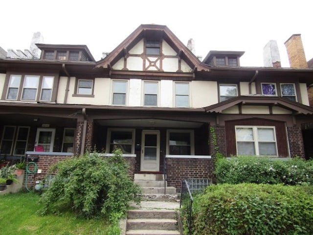 view of front of house featuring stucco siding, covered porch, and brick siding