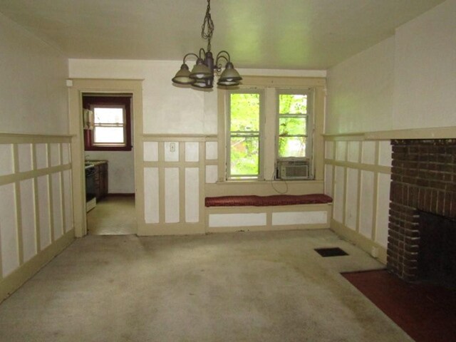 unfurnished dining area featuring carpet flooring, a chandelier, a fireplace, and cooling unit