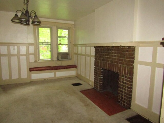 unfurnished living room featuring a chandelier, carpet, cooling unit, a decorative wall, and a brick fireplace