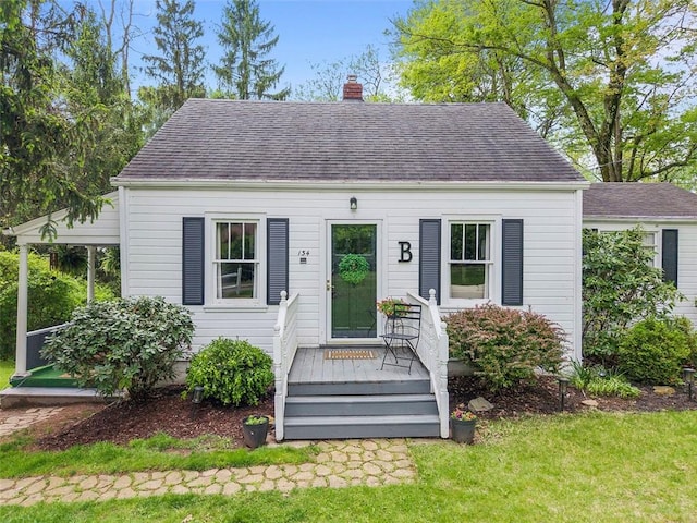 view of front facade featuring a chimney, roof with shingles, a front yard, and a wooden deck