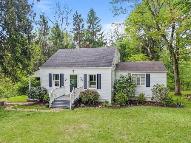 cape cod-style house with a chimney, a front yard, roof with shingles, and a deck