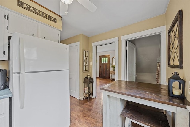 kitchen featuring freestanding refrigerator, wood finished floors, a ceiling fan, white cabinetry, and baseboards