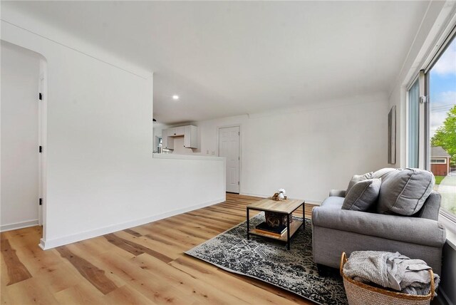 living area featuring light wood-style flooring, baseboards, recessed lighting, and arched walkways