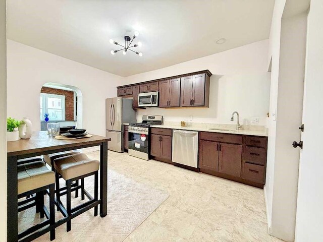 kitchen featuring stainless steel appliances, a sink, arched walkways, dark brown cabinetry, and light countertops