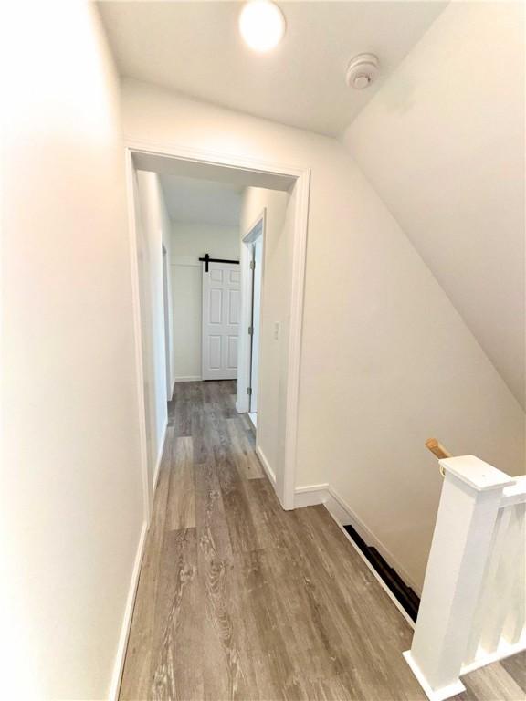 corridor with wood finished floors, baseboards, and an upstairs landing