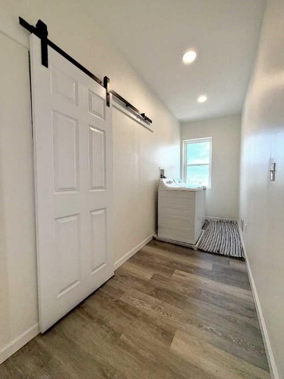 corridor featuring a barn door, wood finished floors, baseboards, and recessed lighting