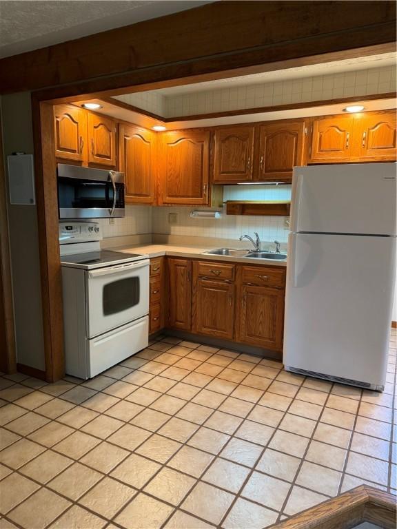 kitchen featuring white appliances, a sink, light countertops, and brown cabinetry