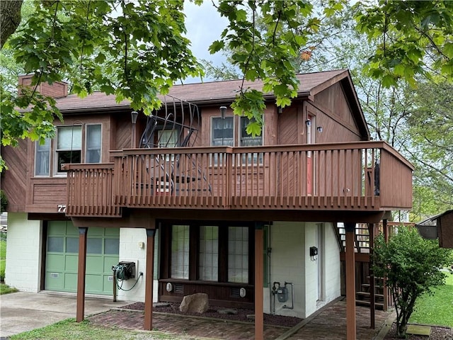 rear view of property with a garage, driveway, concrete block siding, and a wooden deck