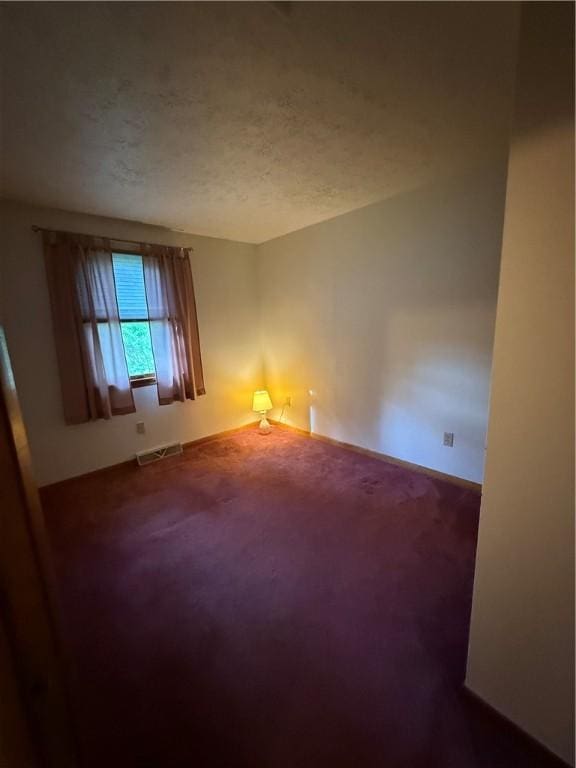 empty room with dark colored carpet, a textured ceiling, and baseboards