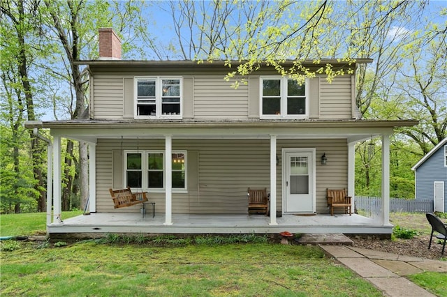 rear view of property featuring a porch, a chimney, and a yard