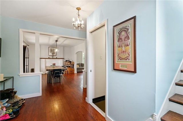 hallway with arched walkways, a chandelier, dark wood-style floors, and baseboards
