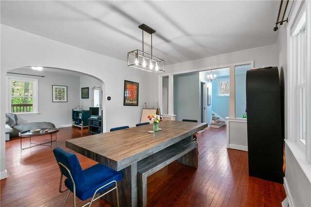 dining area featuring arched walkways, dark wood finished floors, a chandelier, stairs, and baseboards