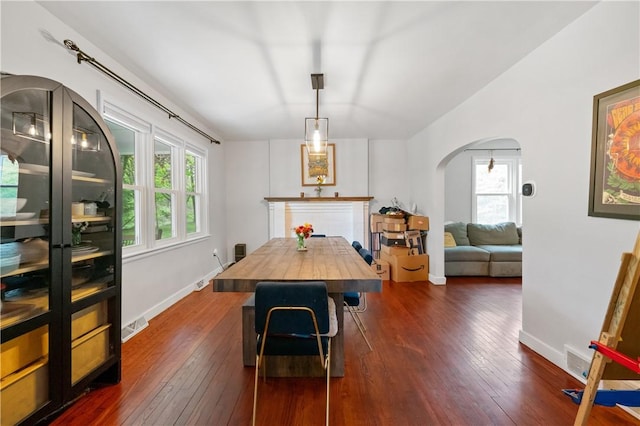 dining area with arched walkways, dark wood-type flooring, and baseboards