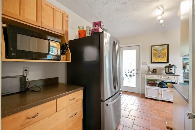 kitchen with black microwave, freestanding refrigerator, dark countertops, light stone finish flooring, and a textured ceiling