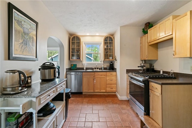 kitchen featuring stainless steel appliances, glass insert cabinets, light brown cabinets, a textured ceiling, and recessed lighting
