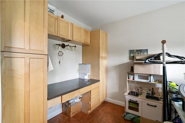 kitchen featuring light brown cabinets, baseboards, and dark tile patterned floors